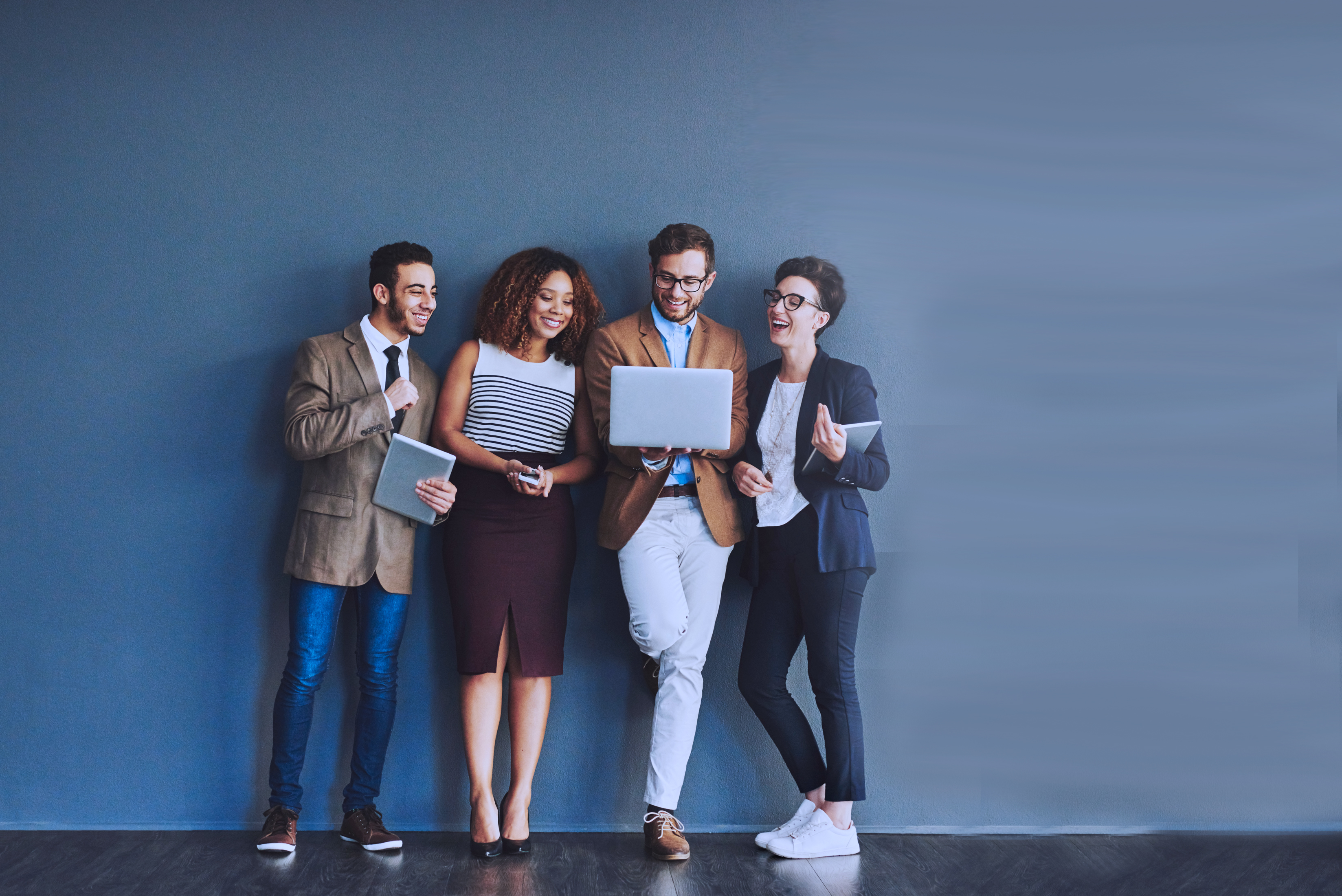 four business people looking at laptop standing in front of blue wall